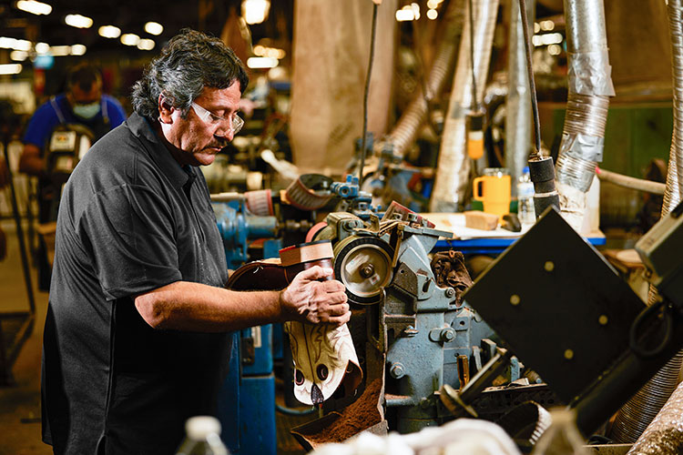 A man holding a boot turned facing a workbench.